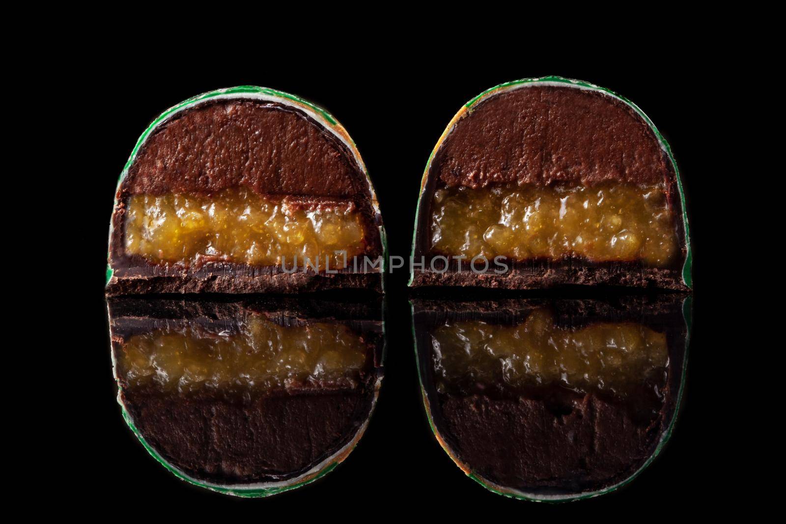 Cut luxury handmade candy with chocolate and yellow confiture filling on black background. Exclusive handcrafted bonbon