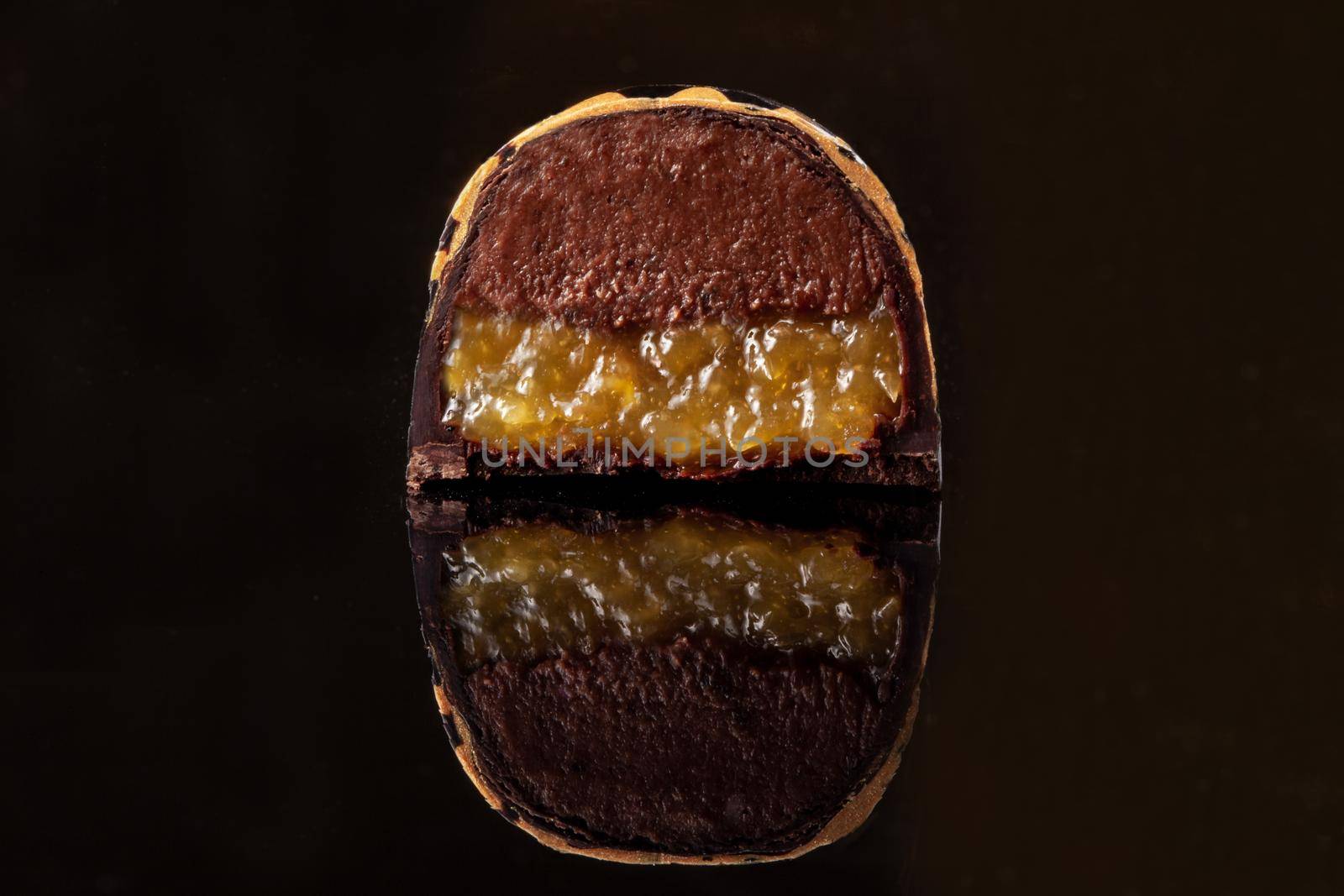 Cut luxury handmade candy with chocolate and yellow confiture filling on black background. by nazarovsergey