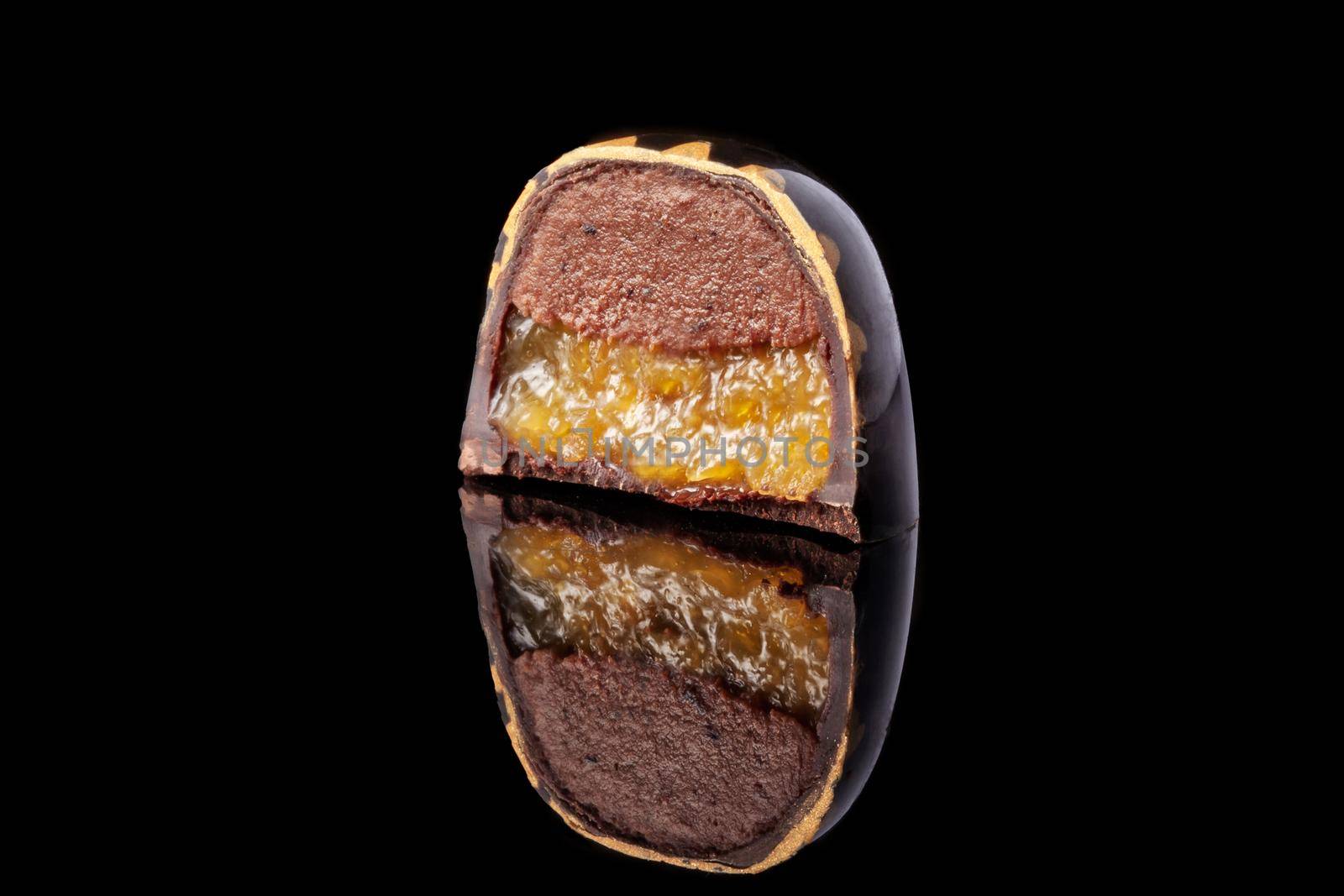 Cut luxury handmade candy with chocolate and yellow confiture filling on black background. by nazarovsergey