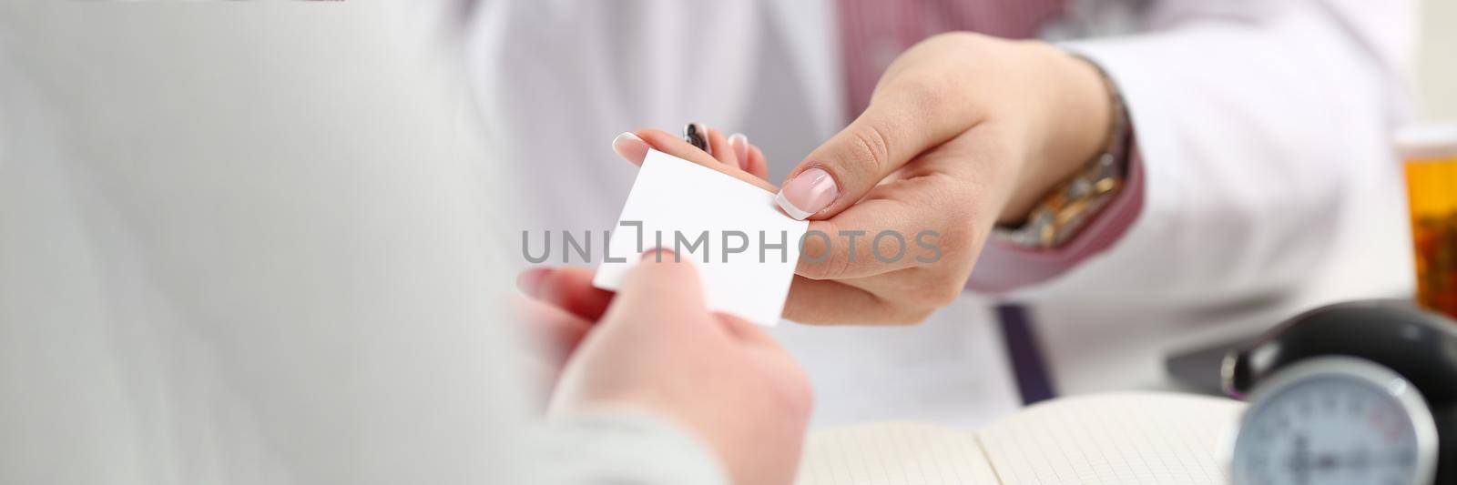 Female doctor hands over white business card to patient. Attending physician choice concept