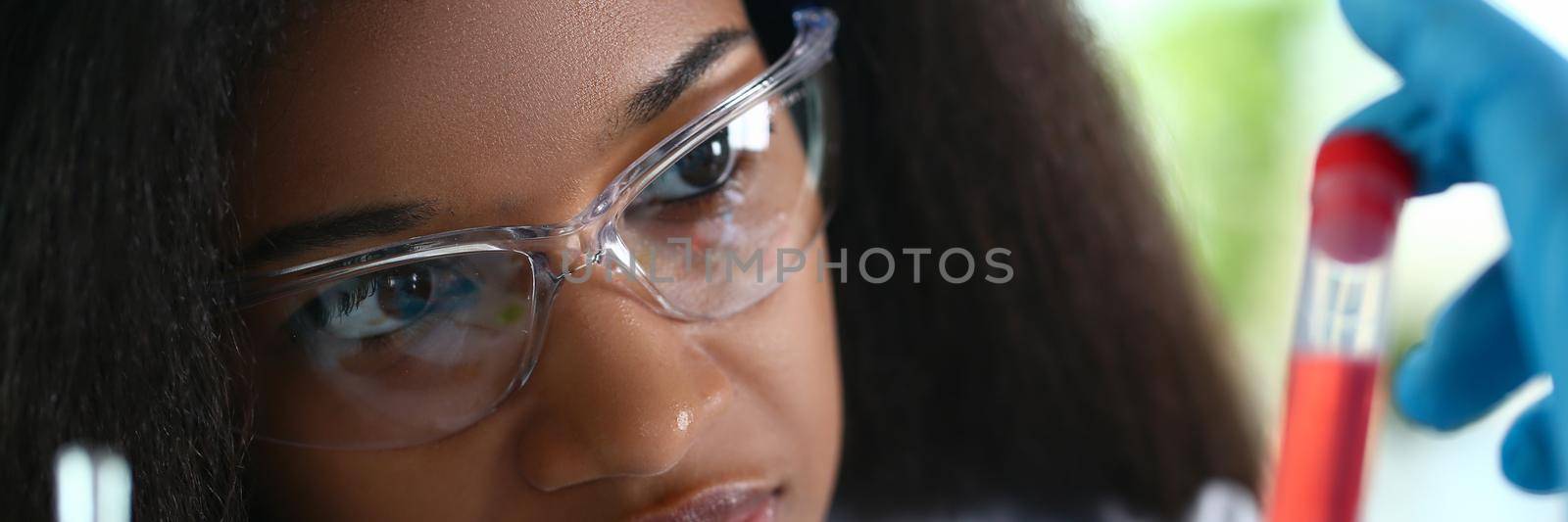 African american chemist holds glass test tube with red liquid solution. Analyzing various reagent options using a chemical manufacturing concept