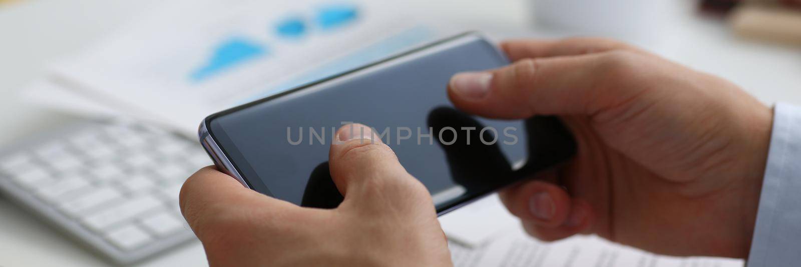 Businessman holds new smartphone in his hand at workplace. Mobile app for business concept