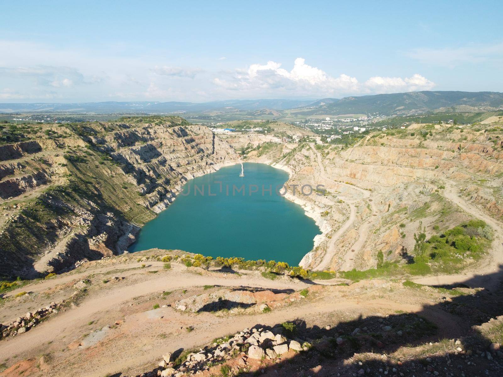 Flight over the turquoise surface of the lake in the center of the quarry. Industrial of opencast mining quarry with flooded bottom. Small lake in the shape of a heart