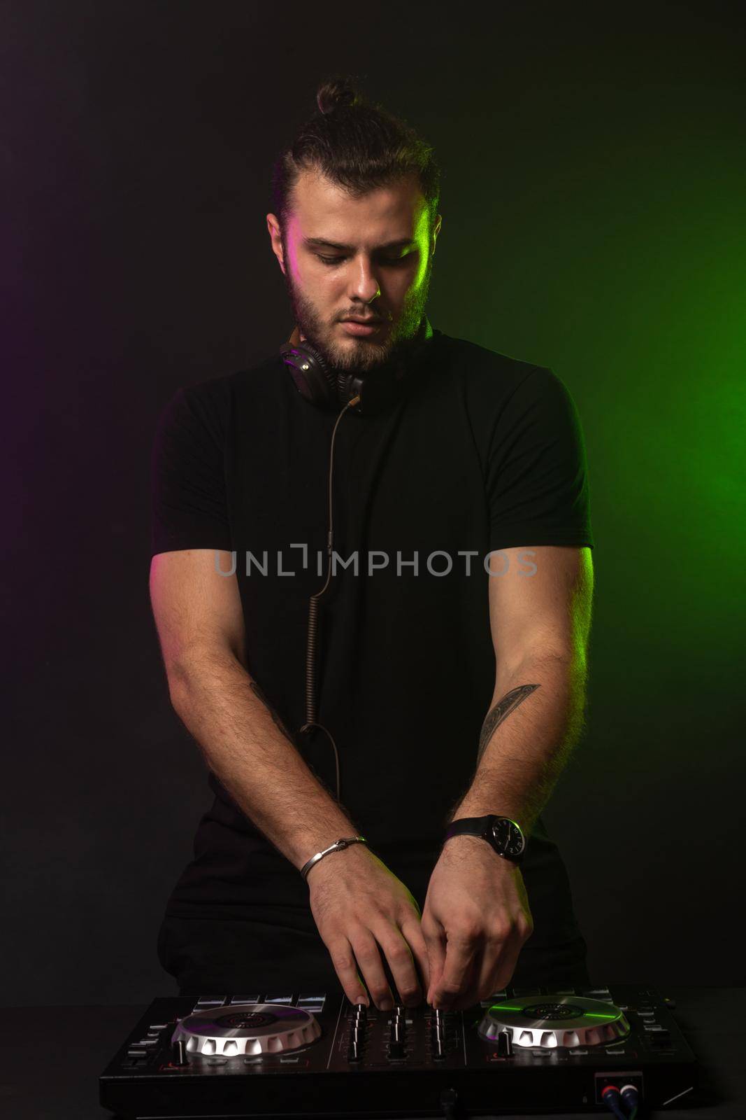 DJ playing music at mixer on colorful foggy background. A fashionable, handsome young man in a black T-shirt is behind the DJ's console. Studio shot