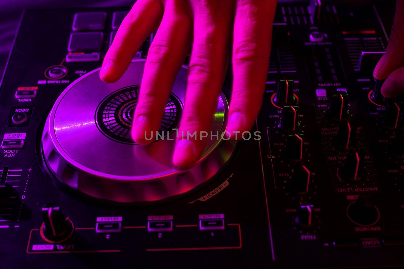 Dj mixing on turntables with color light effects. Soft focus on hand. Close-up. Fun, youth, entertainment and fest concept