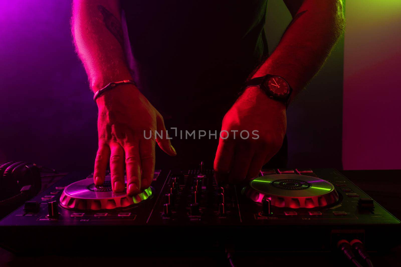 Dj mixing on turntables with color light effects. Soft focus on hand. Close-up. Fun, youth, entertainment and fest concept