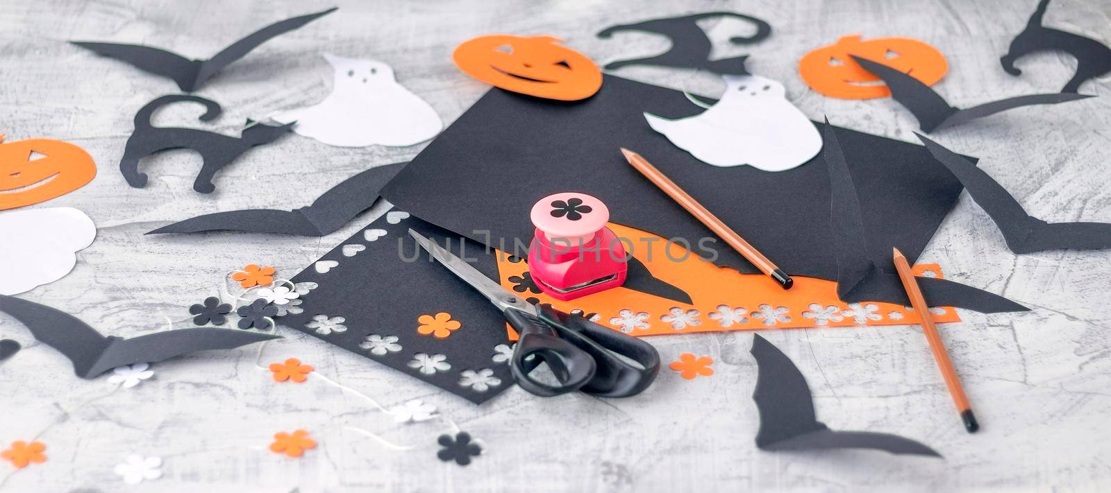 banner with Preparation for Halloween Decoration for the holidays, cutting from colored paper on a white brick wall. orange and black colored paper, scissors, pencils, figured hole punch Soft focus.