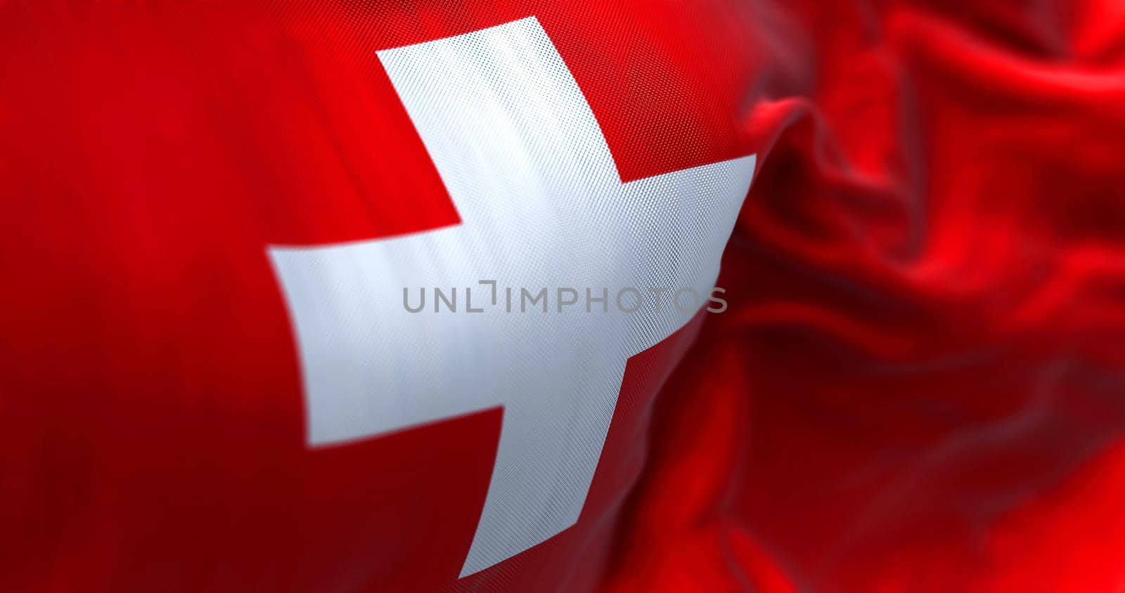 Close-up view of the swiss national flag waving in the wind. Switzerland is a landlocked country located in Europe. Fabric textured background. Selective focus