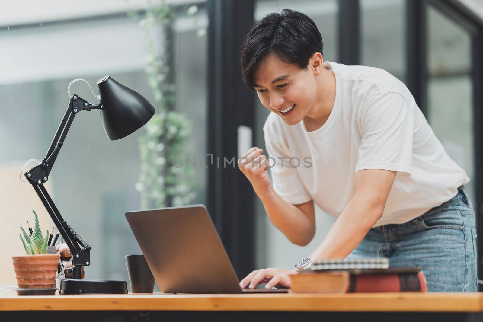 Happy Asian man using laptop computer while have a good news working at office.