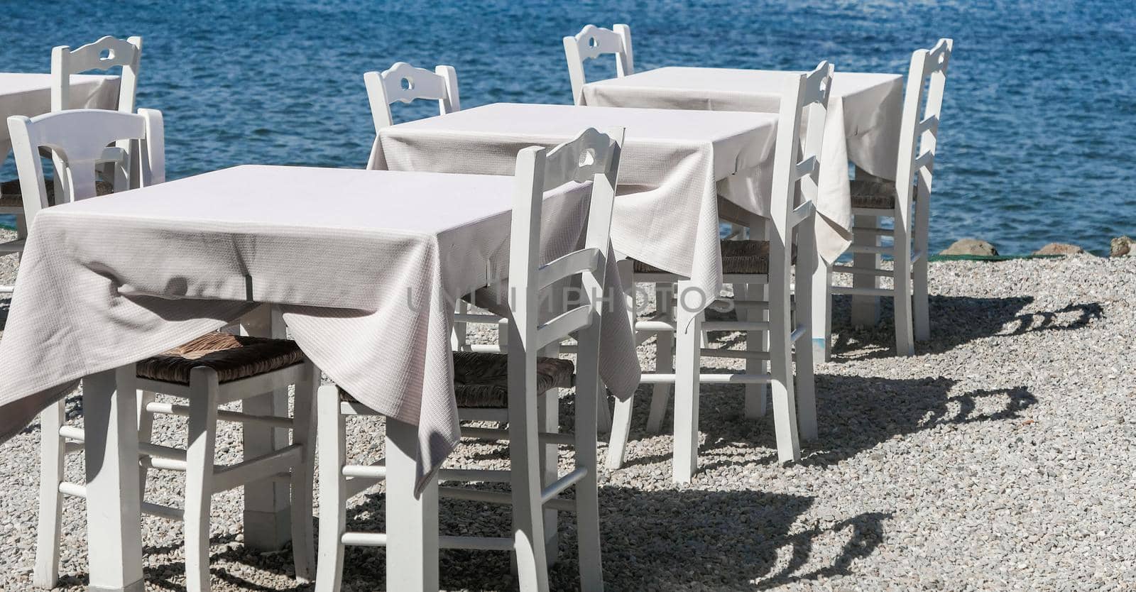 White restaurant tables on the beach in summer - travel, vacation and summer concept. The perfect lunch with a sea view