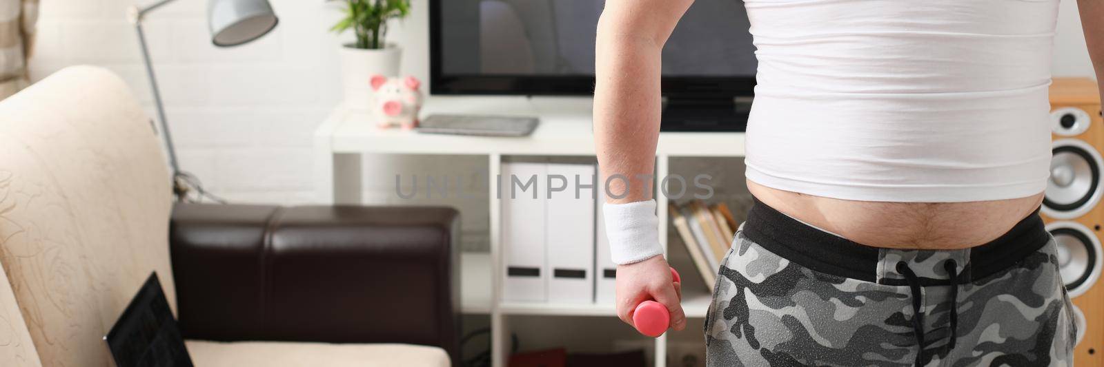 Overweight man is engaged in fitness at home holding dumbbell in hand. Exercise with dumbbells at home concept