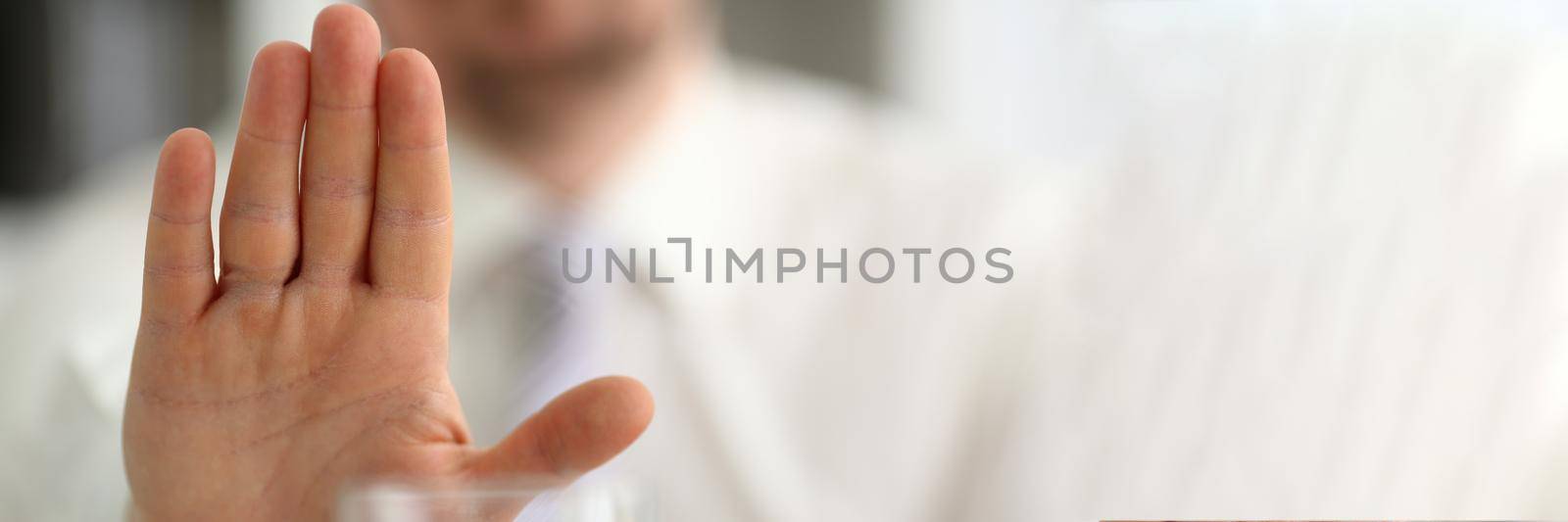 Male hand shows a negative gesture to glass beaker. Refusal of spicy alcoholic drinks concept