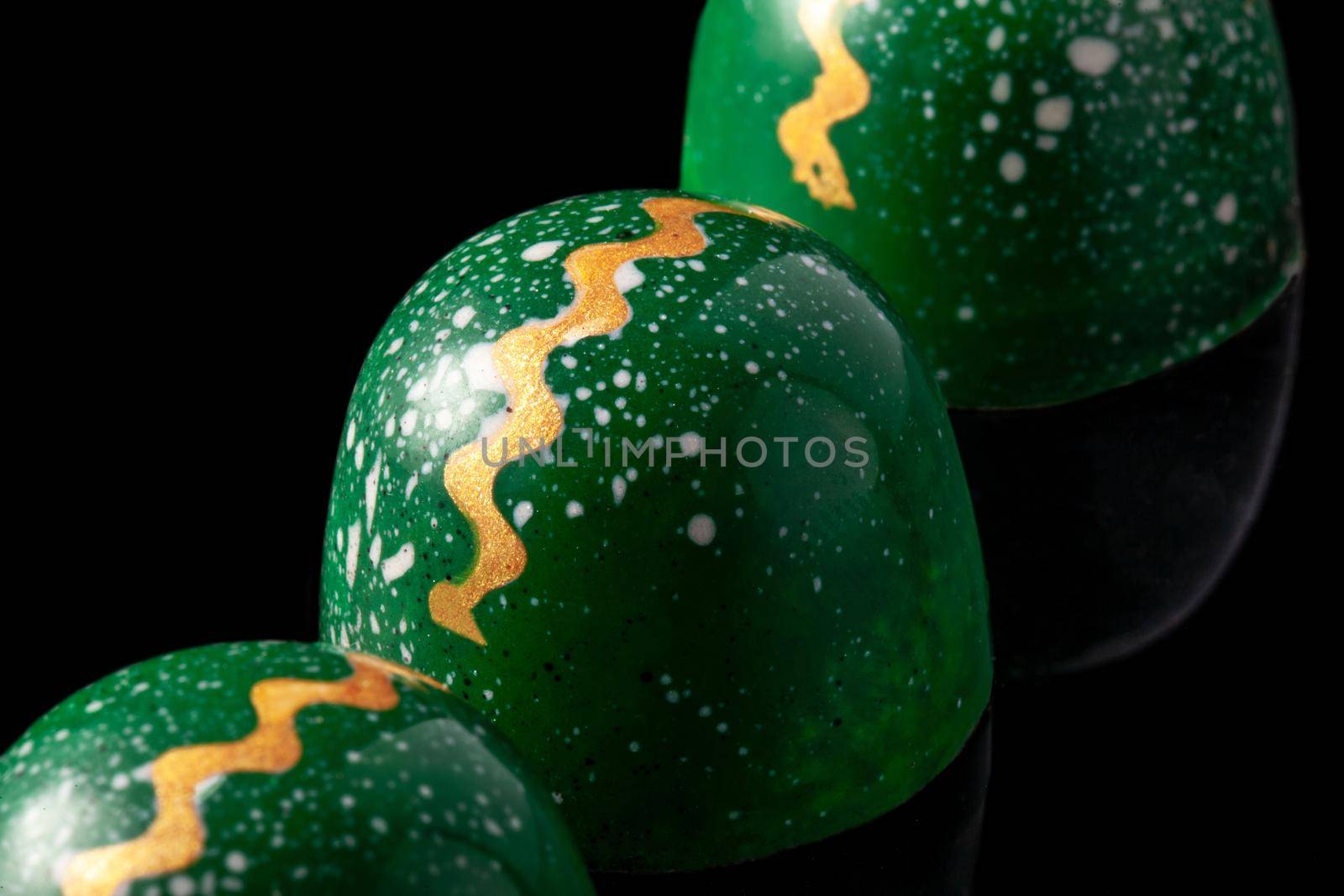 Luxury handmade chocolate candies on black background. Green candies with multicolored drops. Exclusive handcrafted bonbon. Product concept for chocolatier. Close-up