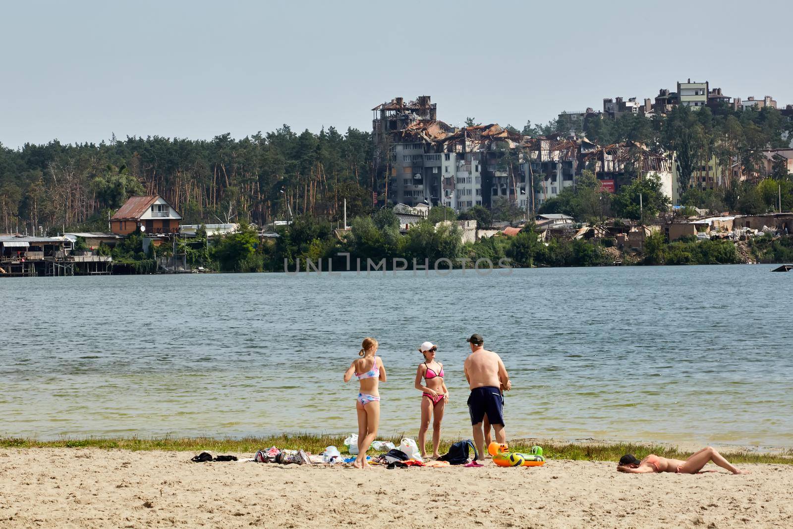 Irpin, Kyiv region, Ukraine - 25 August, 2022: Citi after the Russian occupation. People are having rest near lake opposite destroyed houses