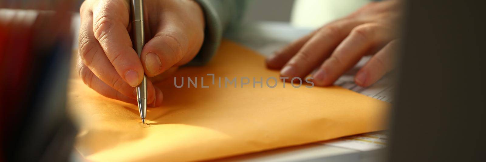 Male hand fills out the address on yellow postage envelope. Delivery and dispatch of mail concept