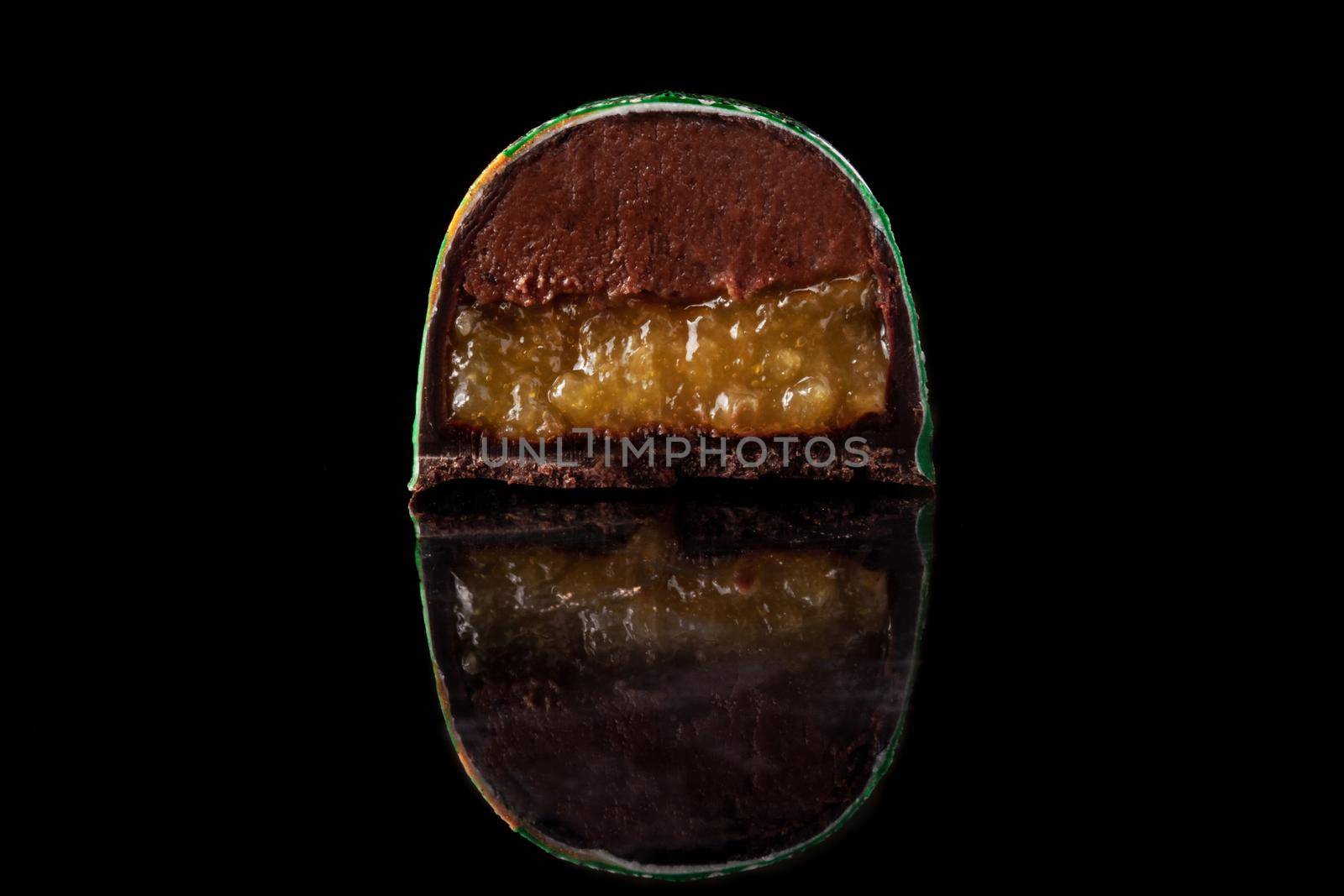 Cut luxury handmade candy with chocolate and yellow confiture filling on black background. Exclusive handcrafted bonbon