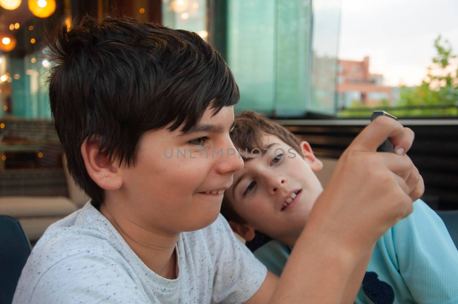 Two boy enjoy playing online games. One boy is watching and waiting. Young boys use their phones for learning in a bar or at home