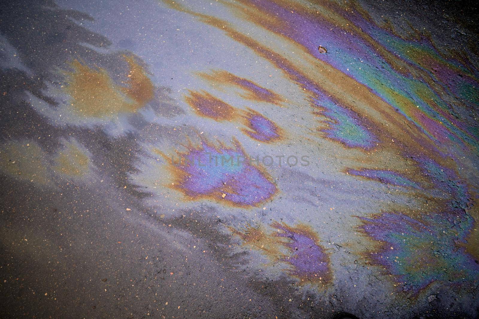 Oil stain on the asphalt, rainbow-shaped colored gasoline stains on an asphalt road as a texture or background