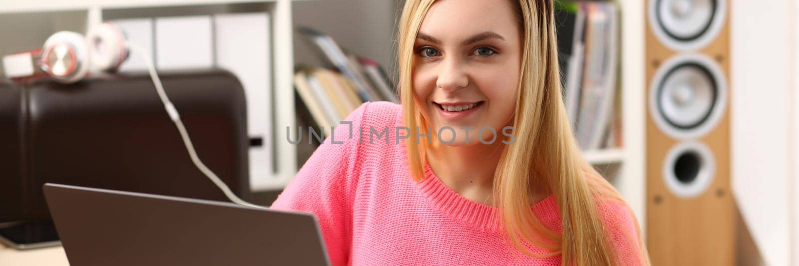 Young smiling blonde woman sitting in living room working on laptop. Remote work and freelance concept