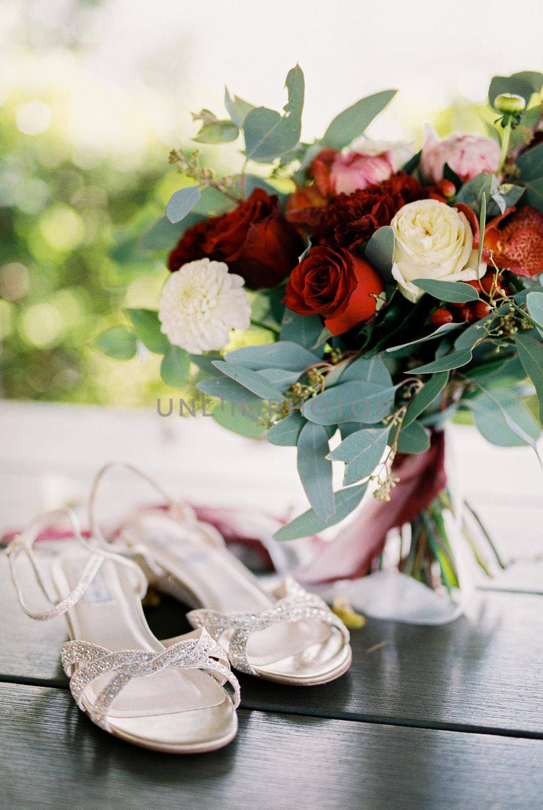 White wedding sandals stand on the table next to the wedding bouquet by Nadtochiy