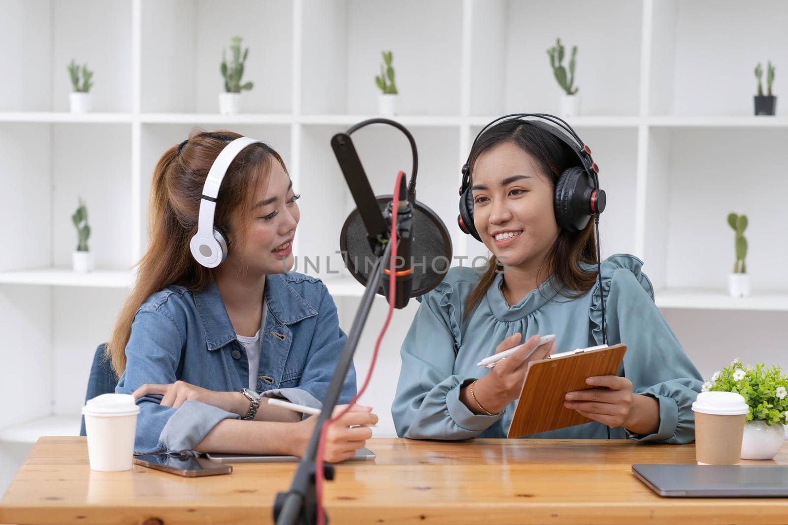 Smile two asian young woman, man radio hosts in headphones, microphone while talk, conversation, recording podcast in broadcasting at studio together. Technology of making record audio concept. by wichayada