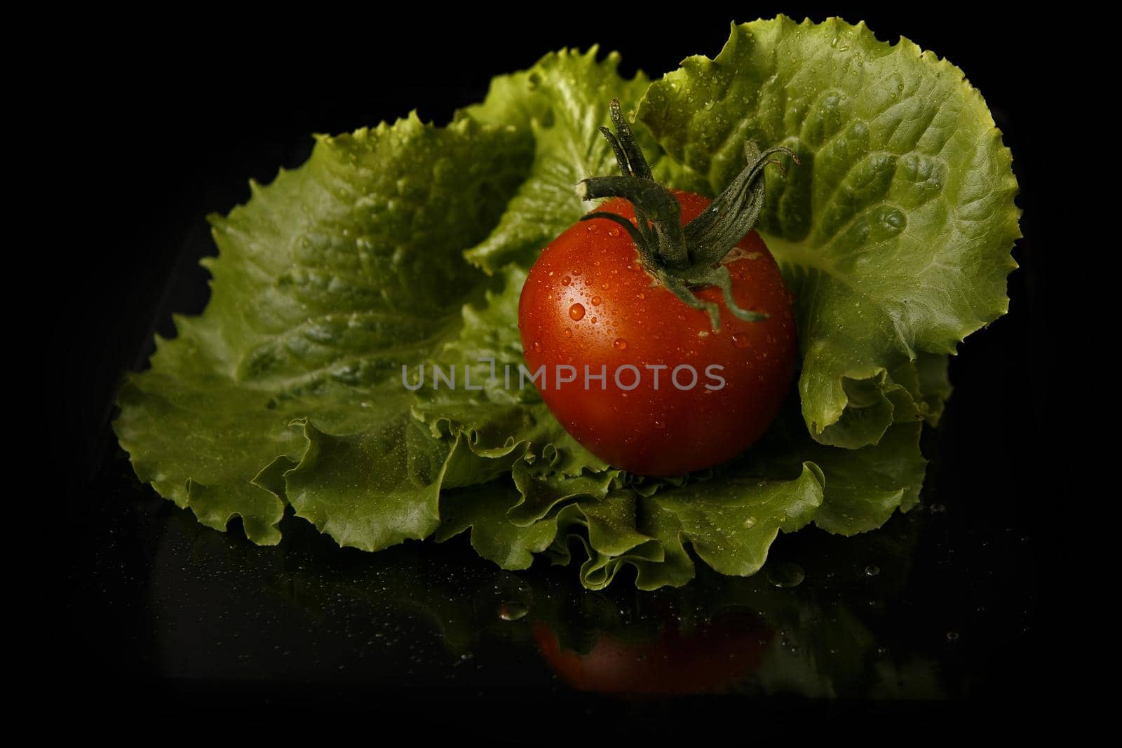 Red tomato fruit on green cabbage leaf on dark background.