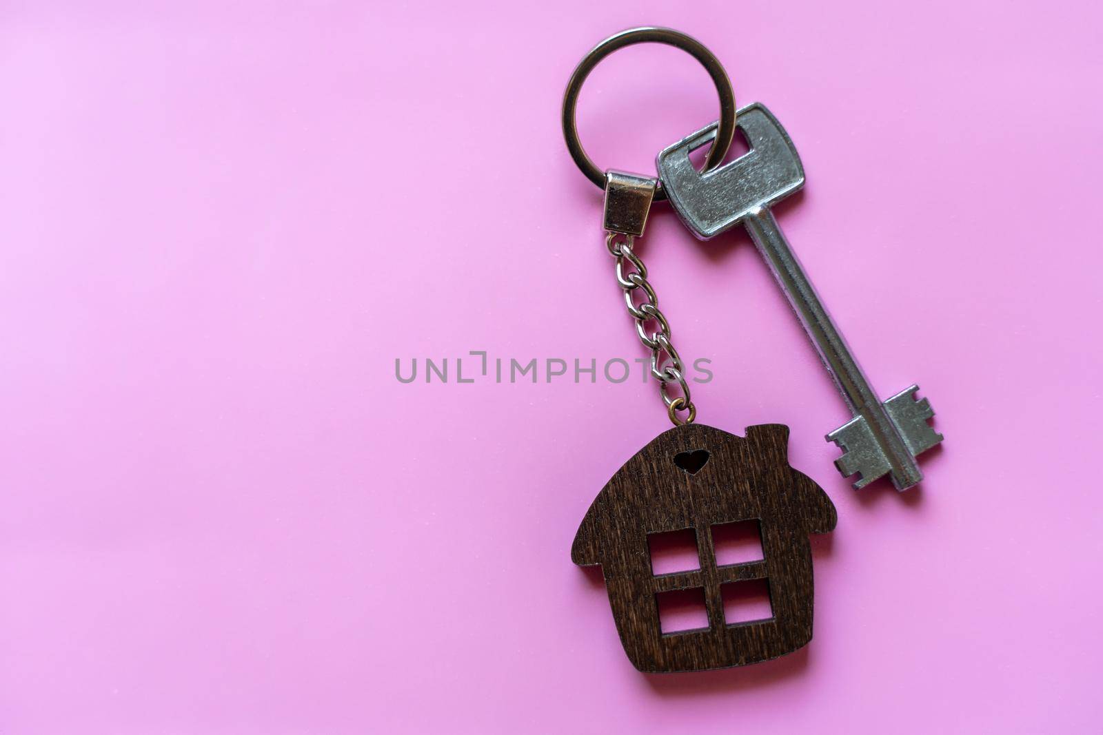 Key with a house keychain on a colored pink background. Real estate agent. Buying a house, apartment. by Matiunina