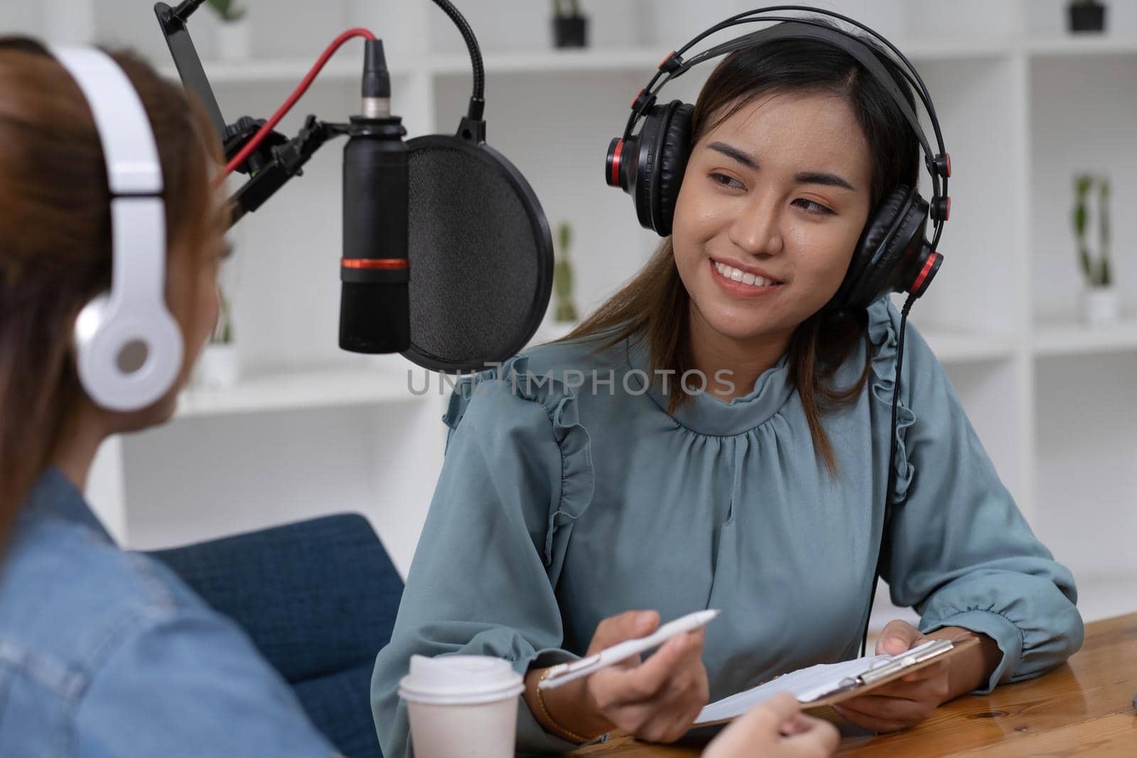 Smile two asian young woman, man radio hosts in headphones, microphone while talk, conversation, recording podcast in broadcasting at studio together. Technology of making record audio concept. by wichayada