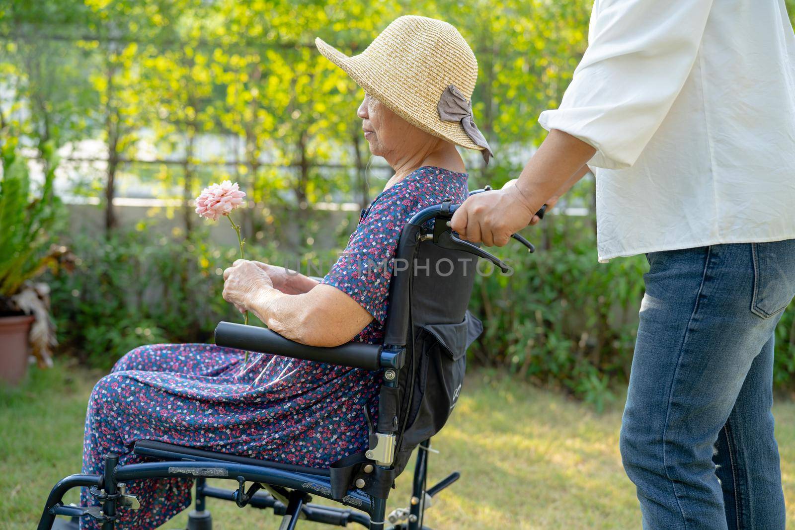 Caregiver help and care Asian senior or elderly old lady woman patient sitting and happy on wheelchair in park, healthy strong medical concept.