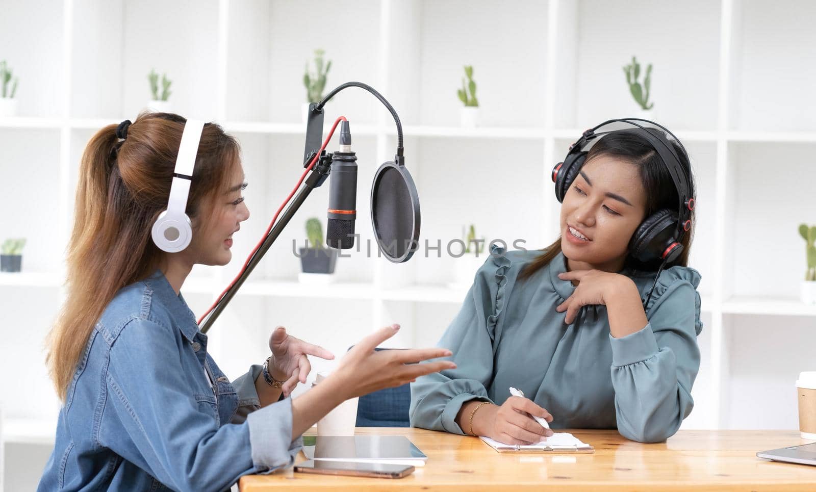 Smile two asian young woman, man radio hosts in headphones, microphone while talk, conversation, recording podcast in broadcasting at studio together. Technology of making record audio concept. by wichayada