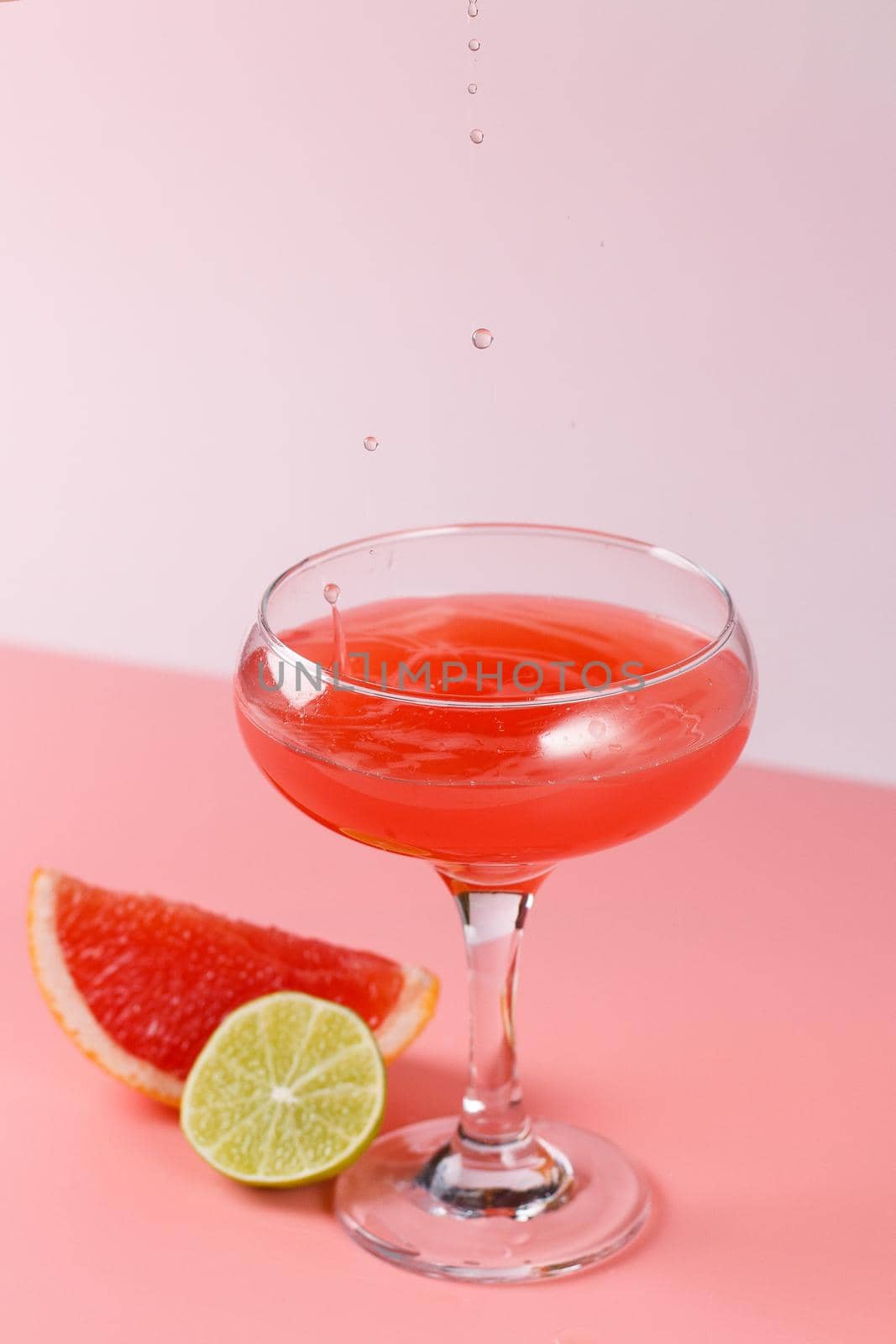 Fresh grapefruit juice with drops falling into a glass on a pink background with grapefruit slices and lime on a pink background. Copy space by lara29