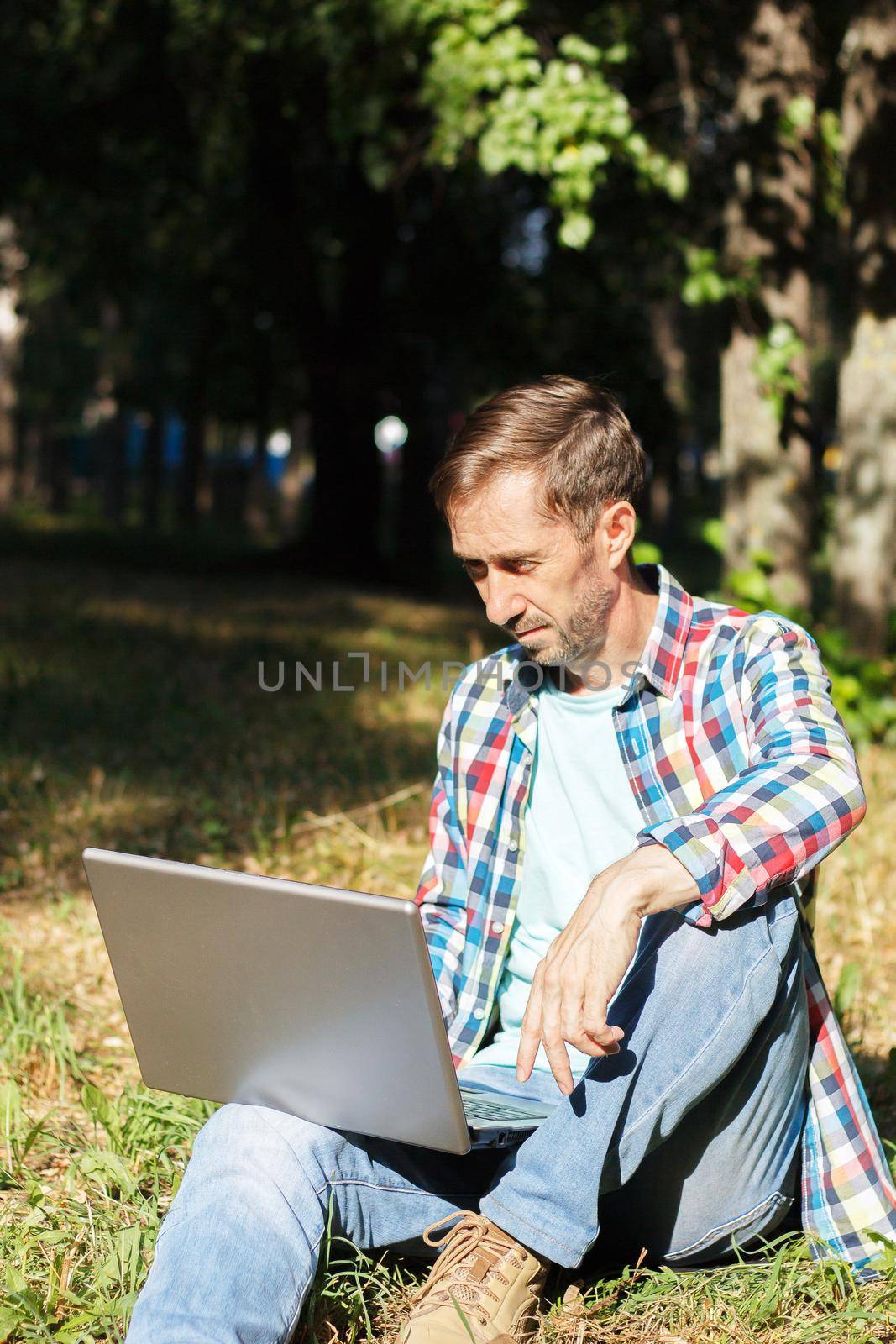 Adult man works on his computer in the park on the lawn.Remote work concept. The writer works remotely, enjoying nature. by lara29