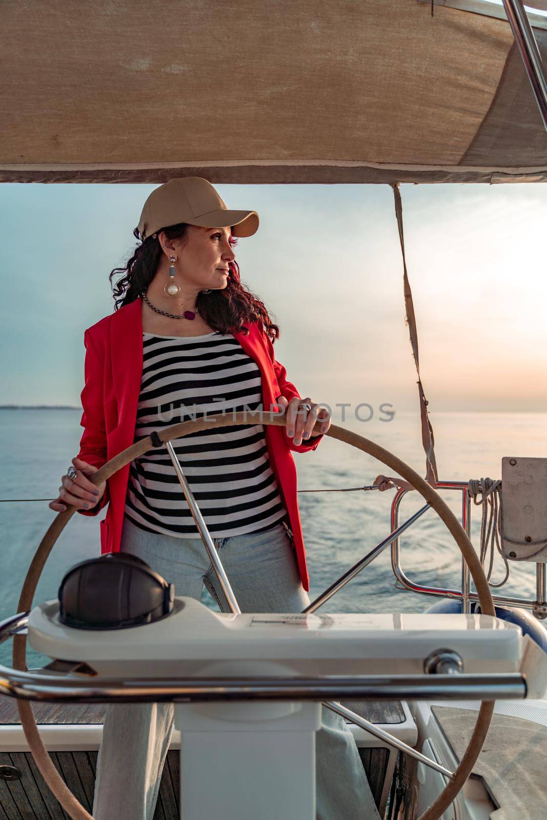 Attractive middle-aged woman at the helm of a yacht on a summer day. Luxury summer adventure, outdoor activities. by Matiunina