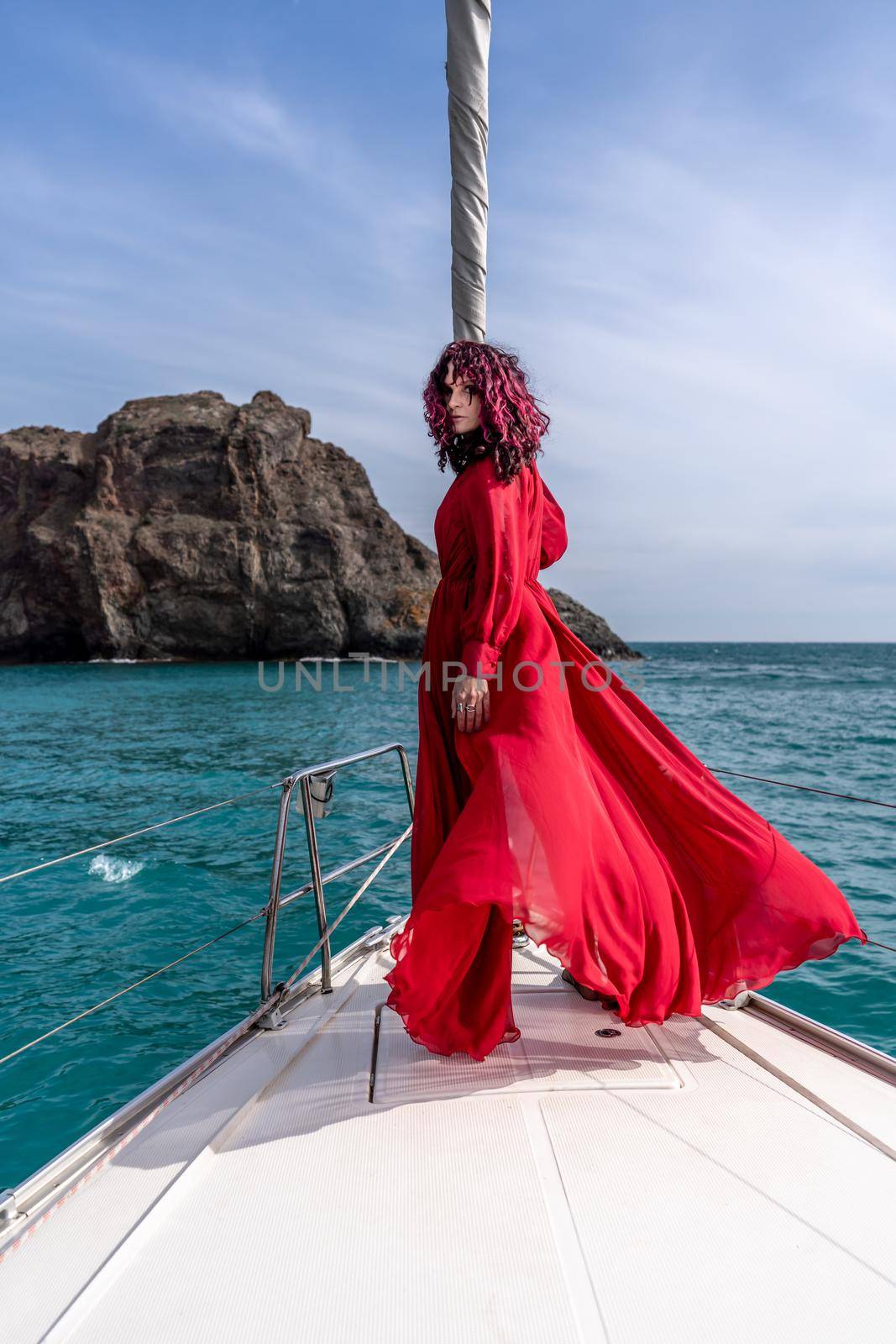 Attractive middle-aged woman in a red dress on a yacht on a summer day. Luxury summer adventure, outdoor activities