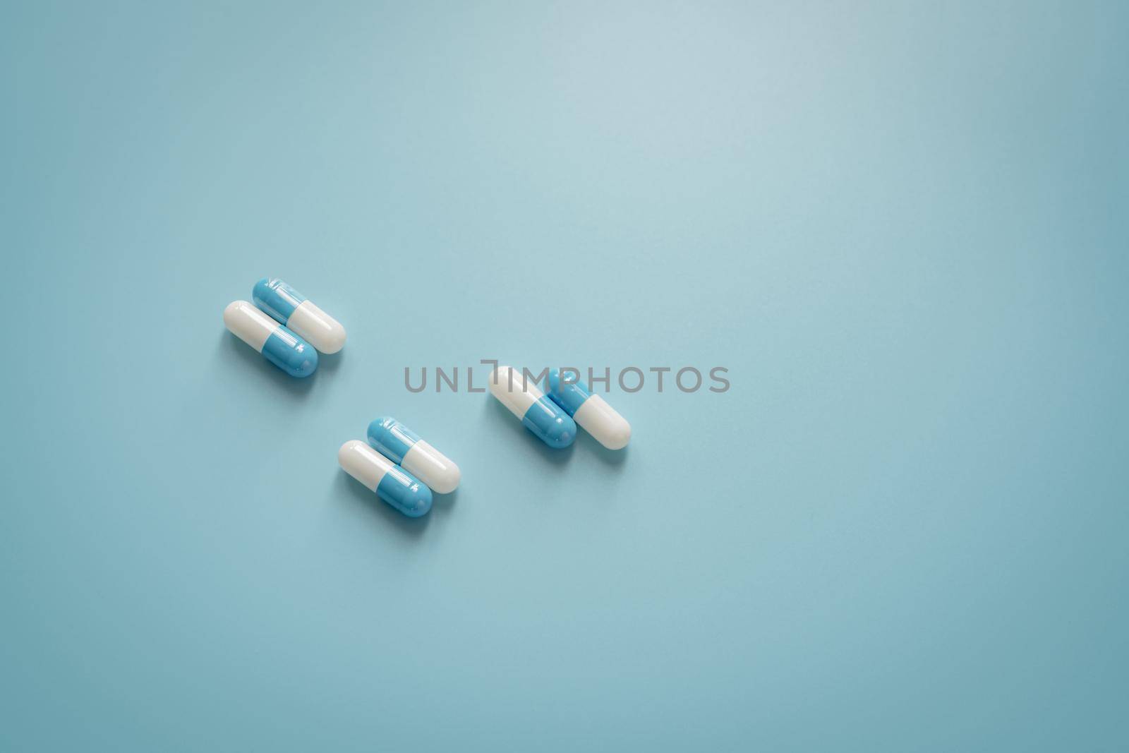 Pairs of white-blue antibiotic capsule pills on blue background. Antibiotic drug. Prescription drug. Pharmacology and recommended dose concept. Pharmaceutical industry. Medical and healthcare concept. by Fahroni