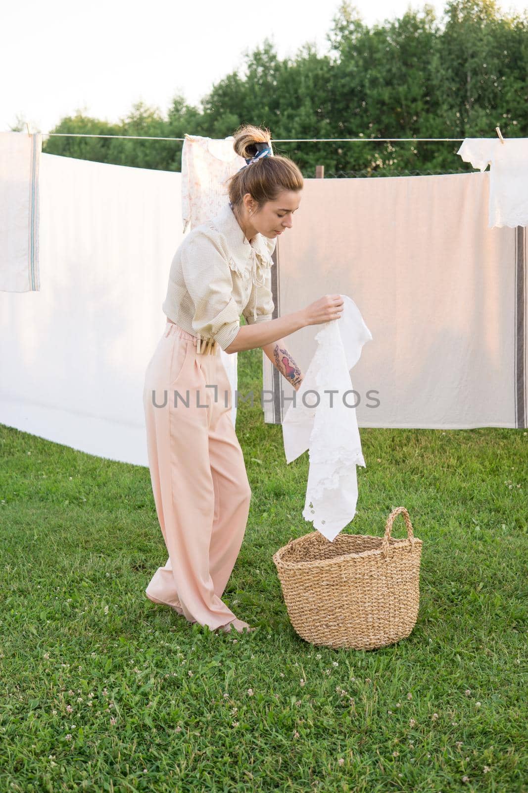 Laundry day. A woman hangs linen and towels on a tree in the courtyard of a village house. Summer cottage concept.