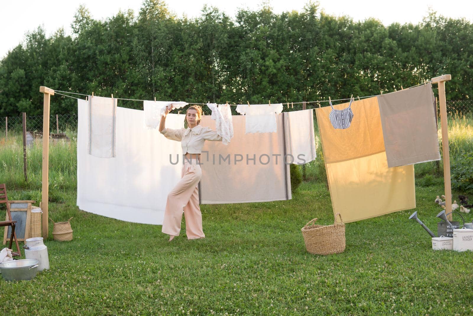Laundry day. A woman hangs linen and towels on a tree in the courtyard of a village house. Summer cottage concept.