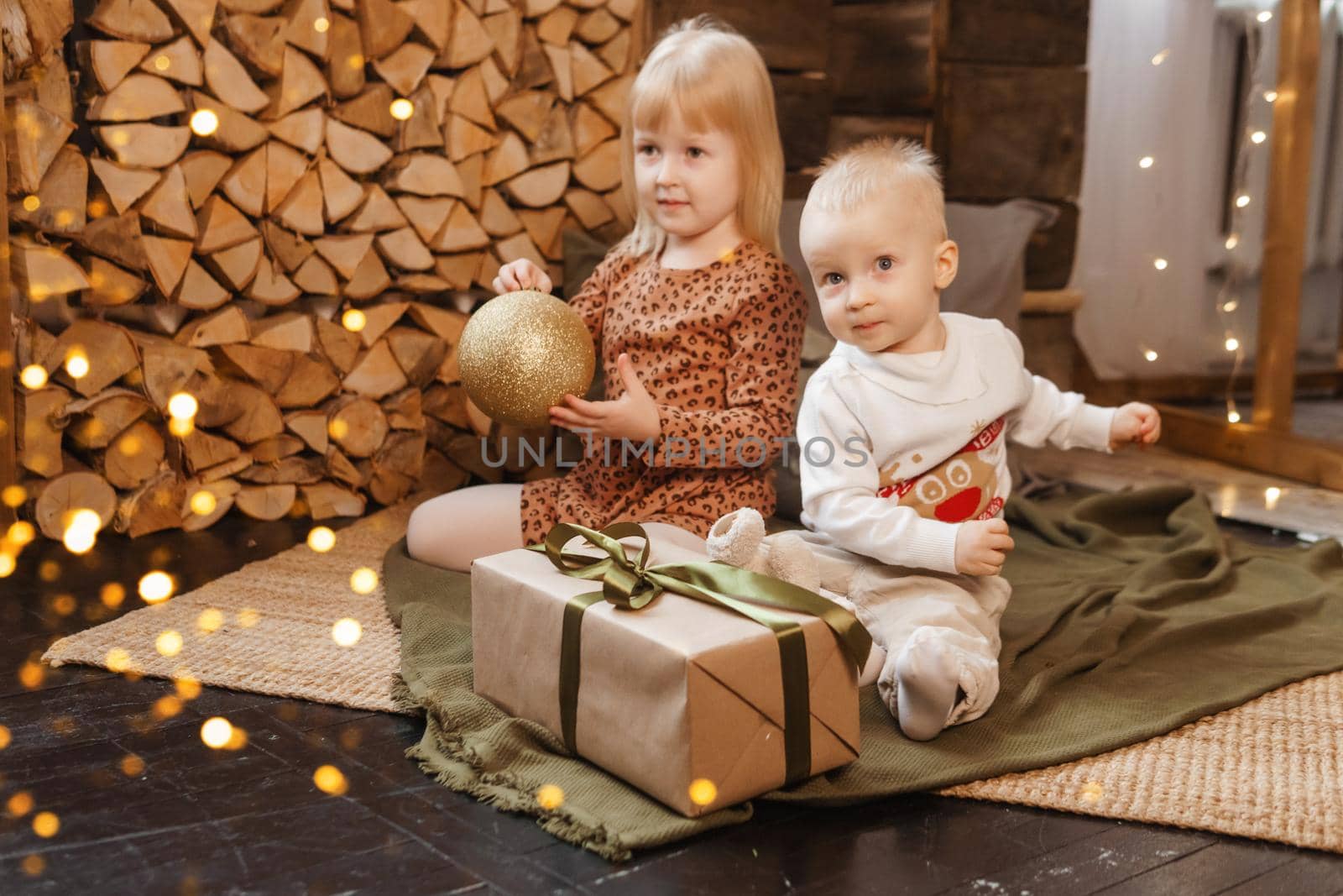 Little brother and sister play on Christmas eve in a beautiful house decorated for the New Year holidays. Children are playing with a Christmas gift. Scandinavian-style interior with live fir trees and a wooden staircase.