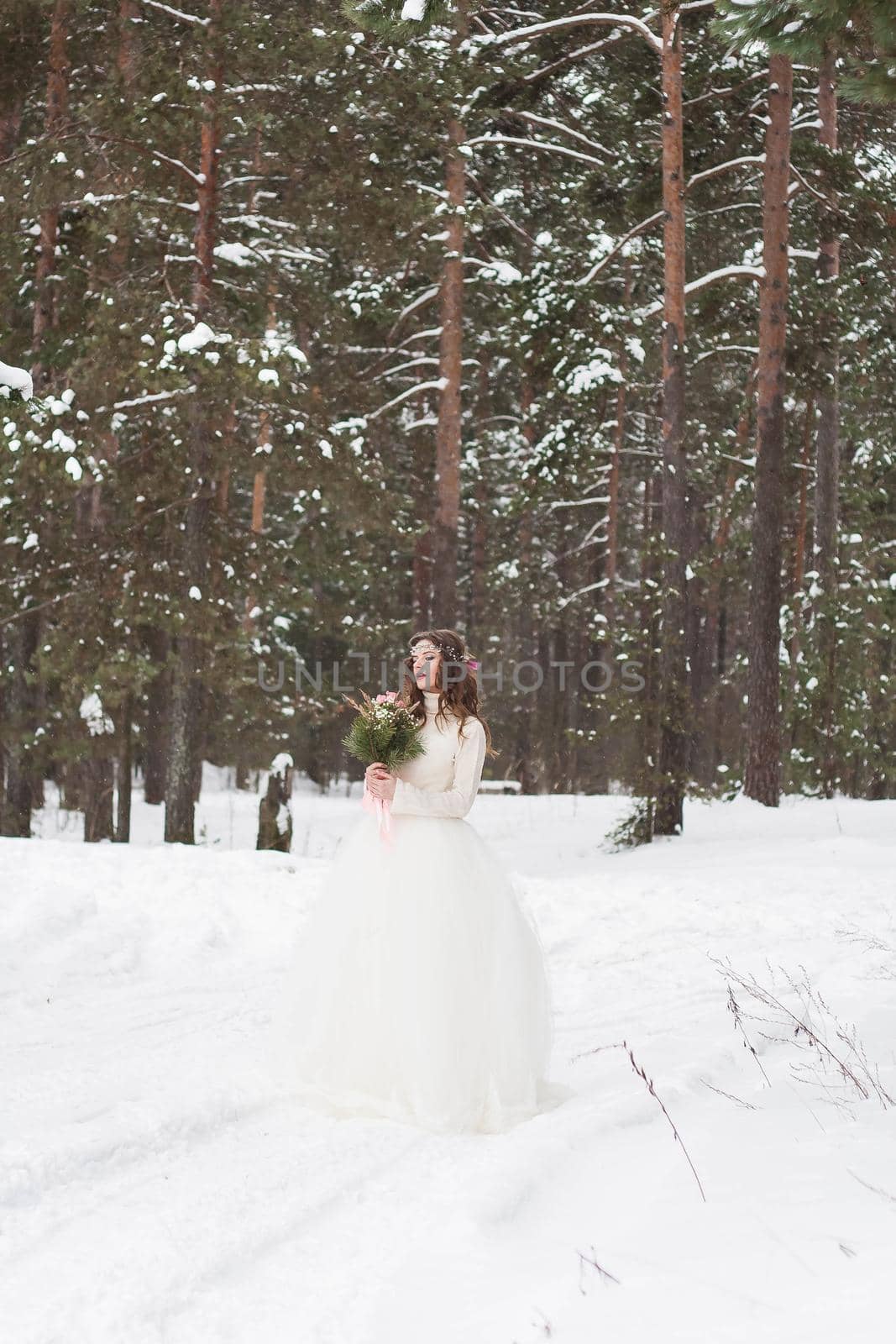 Beautiful bride in a white dress with a bouquet in a snow-covered winter forest. Portrait of the bride in nature.