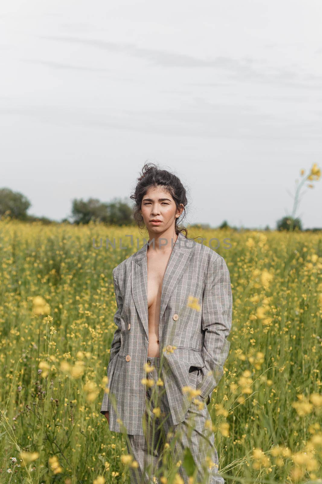 An Asian model poses in a field of yellow flowers for a clothing brand, polyethylene is the main props for a photo shoot. The concept of manufacturing clothing from recycled plastic. A woman in a pantsuit is standing on a plastic bag.