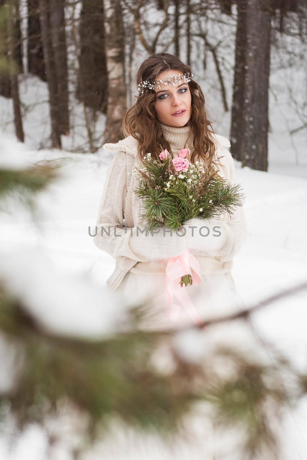 Beautiful bride in a white dress with a bouquet in a snow-covered winter forest. Portrait of the bride in nature.