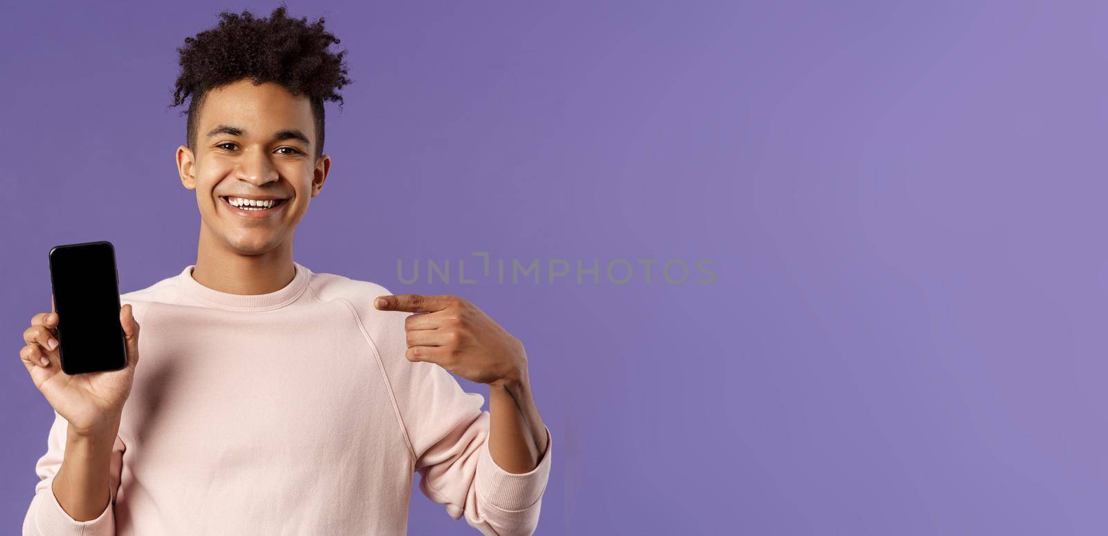 Close-up portrait of young handsome man promoting smartphone app or shopping online, internet delivery for goods, holding mobile phone pointing at display and smiling pleased, recommend by Benzoix