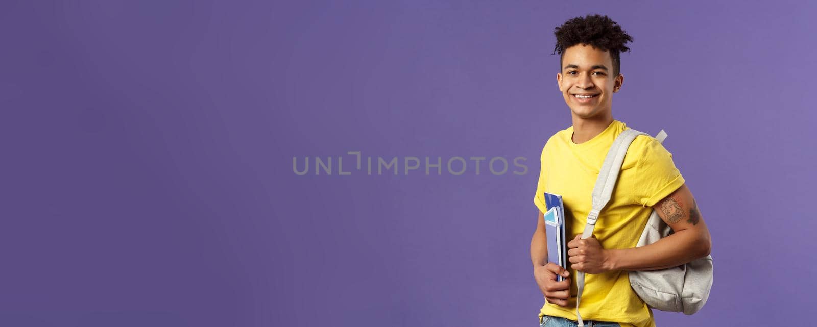 Back to school, university concept. Portrait of handsome charismatic hispanic guy, student walking to campus, going for lecture, studying hold backpack and notebooks, stand purple background.