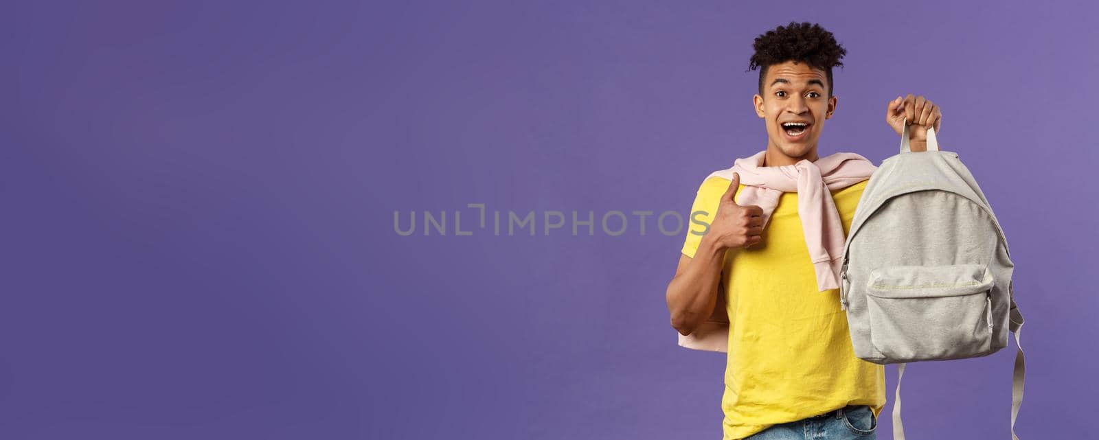 Portrait of cheerful young handsome male student, man recommending backpack, holding rucksack and show thumbs-up, bought new equipment for university semester, purple background by Benzoix