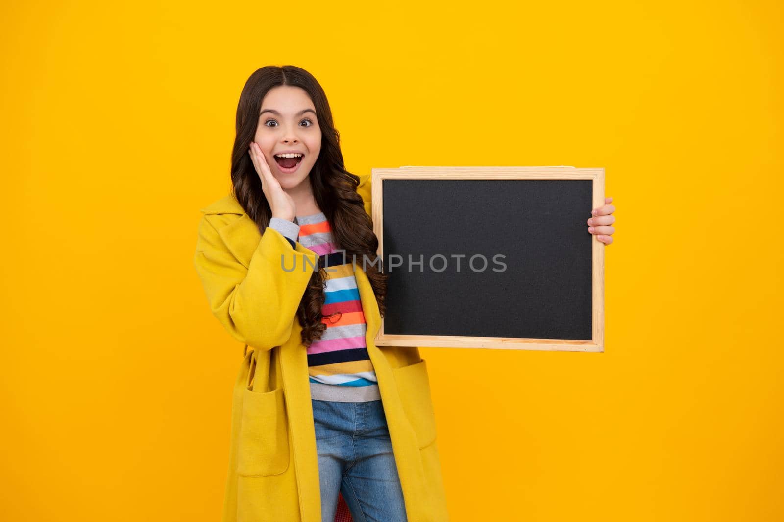 Teenage girl child holding blackboard, isolated on a yellow background. Amazed teenager. Excited teen girl