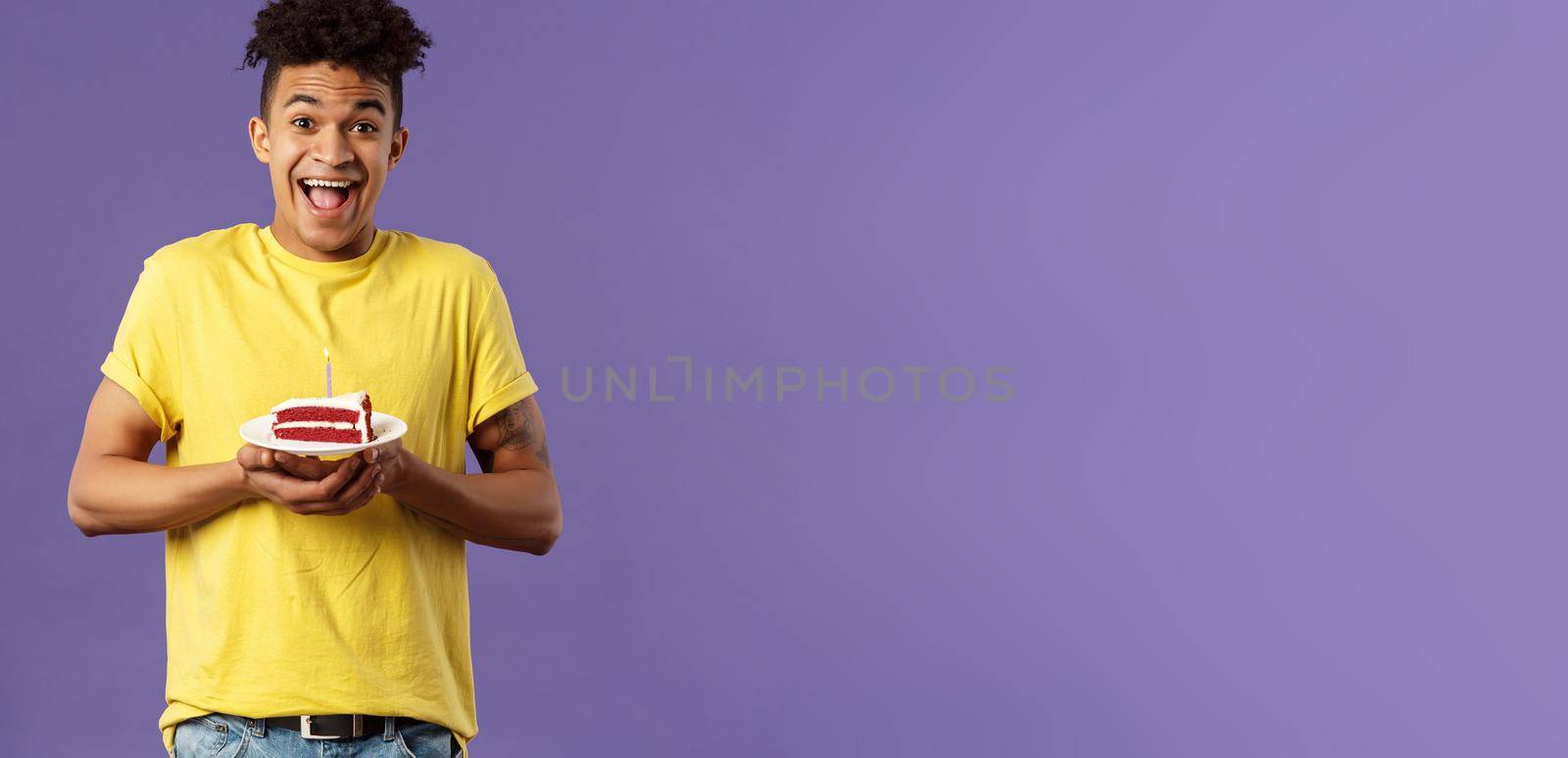 Happy birthday to me. Portrait of upbeat, excited hispanic man with dreads celebrating b-day, holding plate cake with lit candle, smiling amused, making wish, purple background.