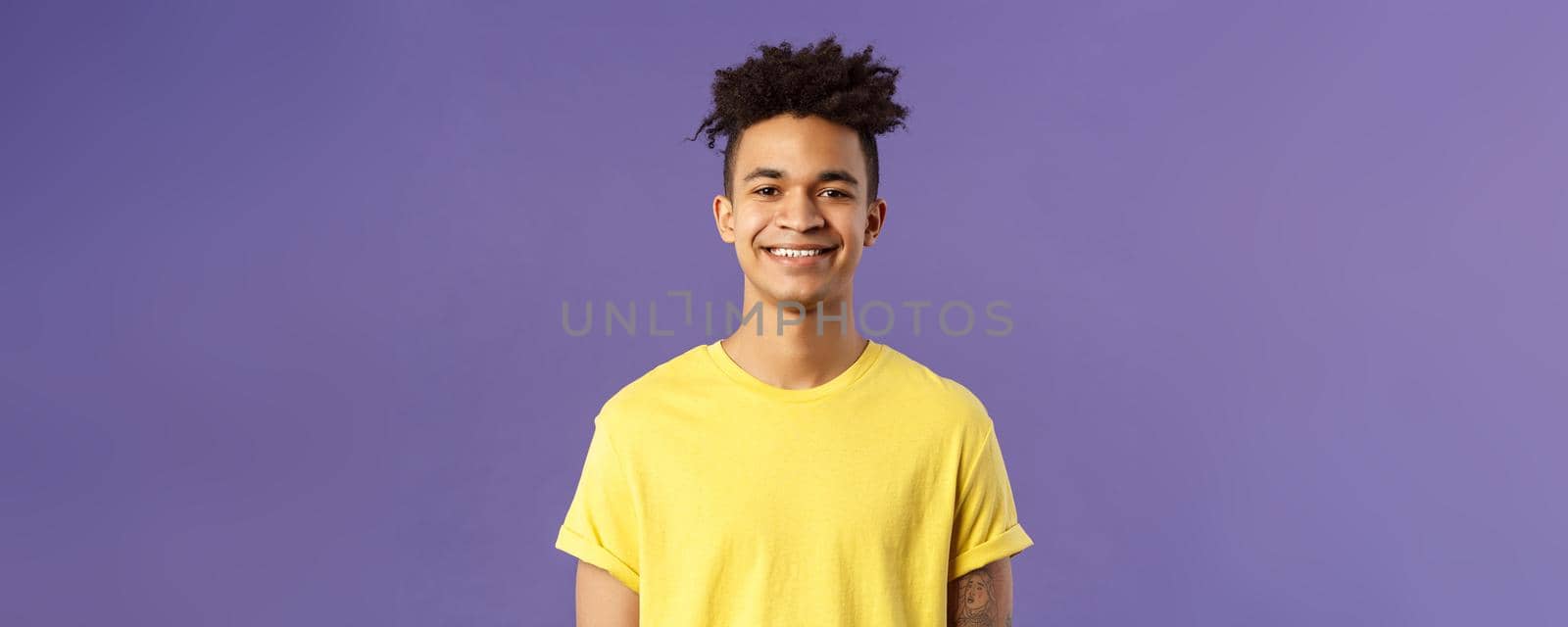 Close-up portrait of nice, friendly-looking hispanic male student in yellow t-shirt, grinning delighted, look upbeat happy and positive, standing enthusiastic with beaming smile purple background.