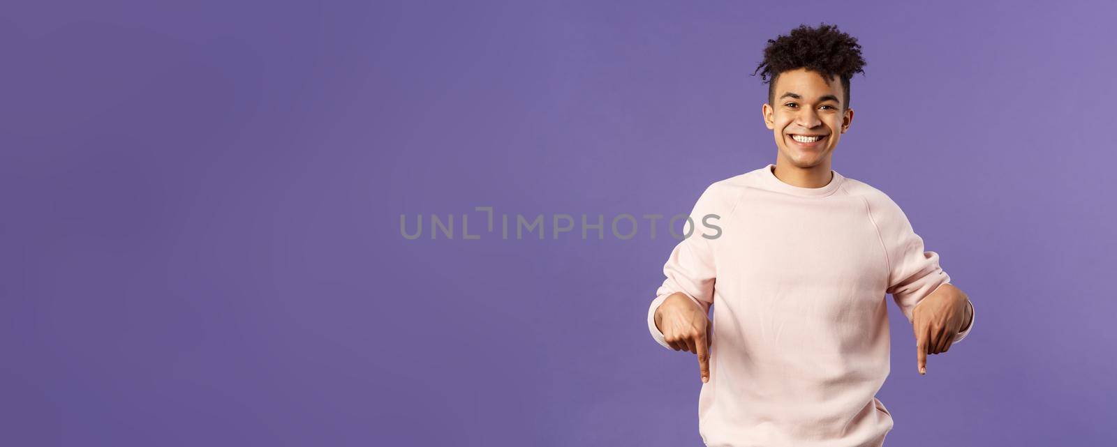 Portrait of cheerful, happy young 25s man recommending product, showing promo of product, delivery service, online shop or appllication, pointing fingers down, smiling pleased camera by Benzoix