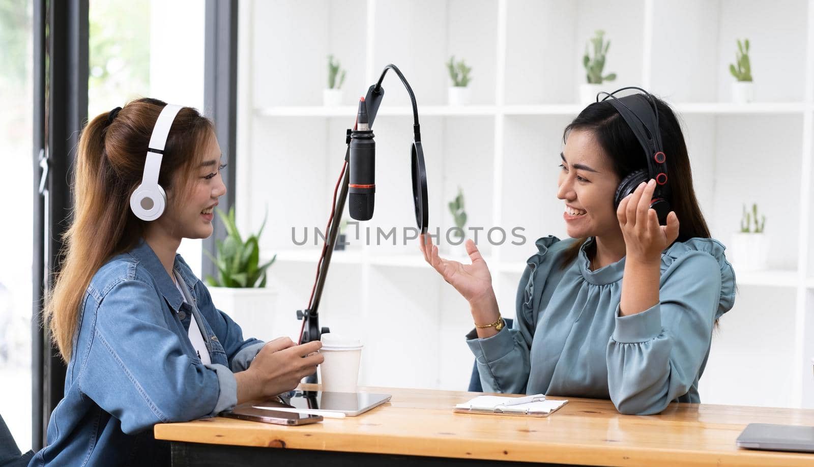 Smile two asian young woman, man radio hosts in headphones, microphone while talk, conversation, recording podcast in broadcasting at studio together. Technology of making record audio concept. by wichayada