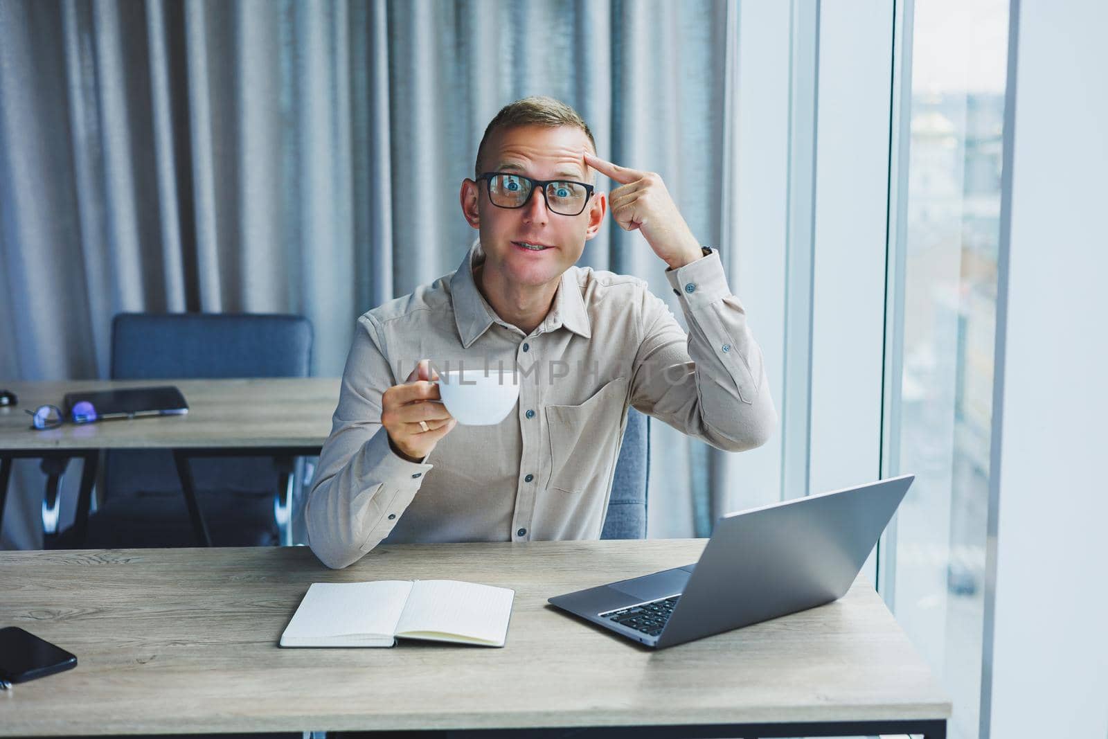 A freelancer in glasses works on a laptop and drinks coffee, a manager sits at a table in the office, works on a laptop. Freelancer workplace, employee at remote work.